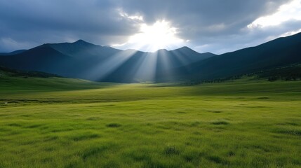 Fototapeta premium Radiant sunlight breaks through clouds over a vast meadow, surrounded by mountains