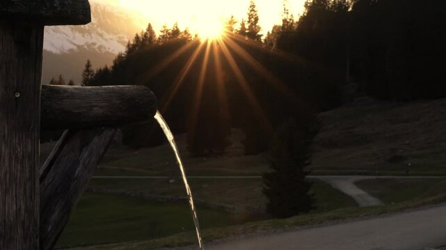 Pure water flows from a wooden pipe into an old trough in a mountain landscape