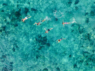 Aerial view of a family snorkeling in crystal-clear turquoise waters above a coral reef near Phi Phi Island, Thailand.