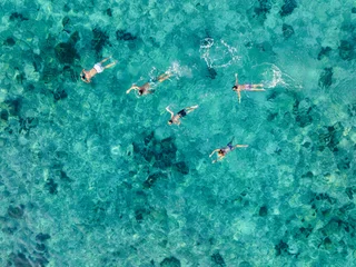 Aerial view of a family snorkeling in crystal-clear turquoise waters above a coral reef near Phi Phi Island, Thailand. © Travel Wild