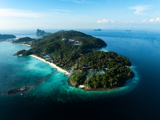 Aerial view of Phi Phi Don island in Thailand with lush green hills, turquoise bays, white sand beaches, and boats along the coastline under a clear blue sky.