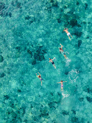 Top-down view of a group of people swimming over a vibrant coral reef in shallow tropical waters near Phi Phi Island, Thailand.