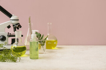 Laboratory glassware and microscope with ingredients for preparing natural cosmetics on white table near pink wall