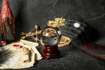 Bloody witch hand with crystal ball, dry flowers and magic attributes on grunge black background....