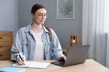 Woman taking notes during online lesson at table indoors. Self-study