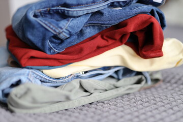 A pile of clothes, including jeans and a red shirt, are stacked on top of each other