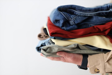 A person is holding a pile of clothes, including jeans and a red shirt. The clothes are piled on...