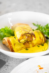 Two vibrant, rolled crepes filled with savory ingredients are topped with a rich yellow sauce and served alongside fresh greens. The dish exudes an inviting culinary appeal.
