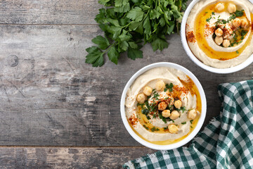 Chickpea hummus with olive oil, parsley and paprika in bowl on wooden table. Top view. Copy space