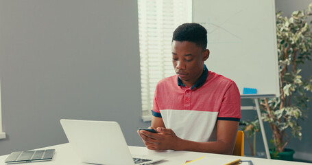 An experienced salesman sits at desk in office, laptop stands in front of him, man with dark complexion dials number, calls customer, talks on phone, places an order, enters data into the system