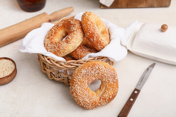 Wicker bowl of tasty bagels with sesame seeds on white background