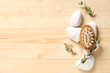 Composition with bottle of cosmetic product, massage brush, spa stones and eucalyptus branches on wooden background