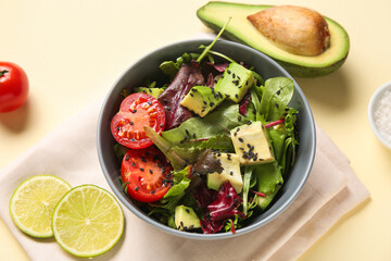 Bowl of tasty avocado salad with cherry tomatoes and slices of lime on yellow background