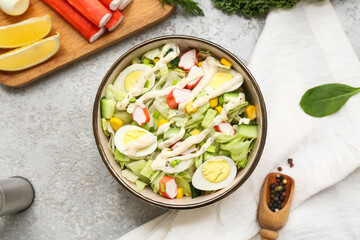 Bowl of salad with crab sticks, iceberg leaves, corn, quail eggs and cucumber on grey grunge background