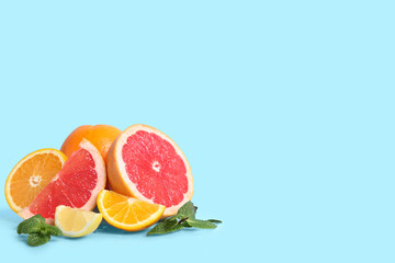 Different cut citrus fruits with mint leaves on blue background