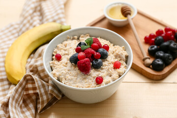 Bowl with tasty oatmeal and berries on wooden background