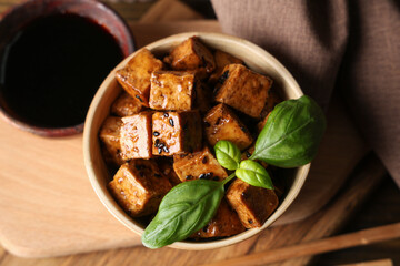 Bowl with pieces of fried tofu cheese and basil on wooden background, closeup