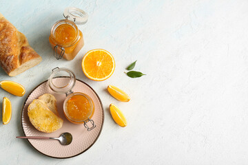 Jars of sweet orange jam and slices of bread on light blue background