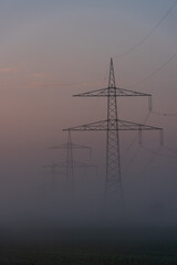 Electrical grid towers in a row on a foggy morning in a german village