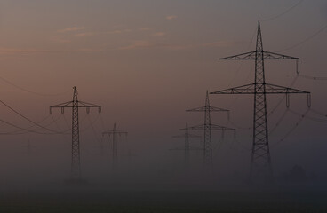 High voltage towers in a row on a foggy morning in a german village