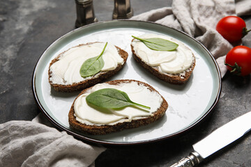 Plate of tasty bruschetta with processed cheese, spinach leaves and fresh tomatoes on black background. Closeup