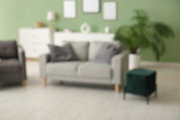 Armchair, cozy sofa and pouf in interior of living room. Blurred view