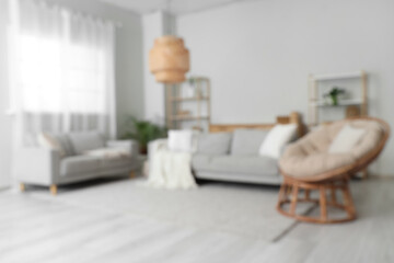 Blurred view of stylish living room with cozy armchair, grey sofas and wicker lamp