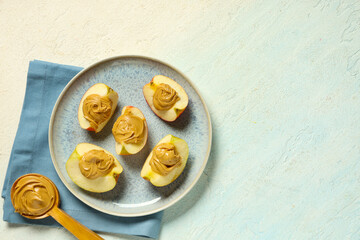 Plate of tasty apple wedges with nut butter and wooden spoon on light background