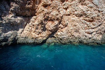 Turquoise water at the foot of the mountain, close-up. Beautiful view of the azure waters washing part of the cliff off the coast of the island.