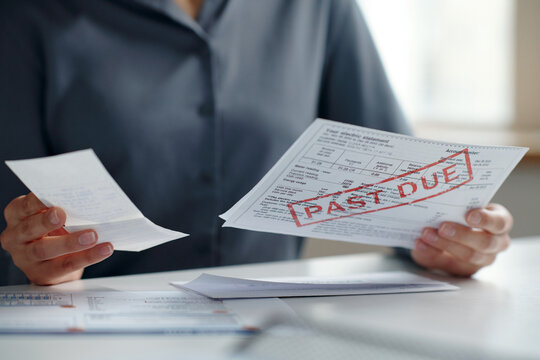 Close up of bills with past due notice with unrecognizable woman filing taxes from home copy space