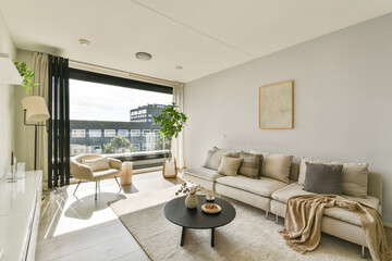 A stylish modern living room featuring a comfortable sofa, decorative elements, and large windows allowing natural light to flood the space, creating a cozy atmosphere.