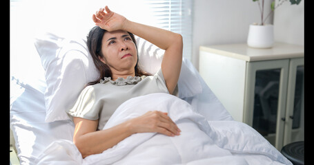 A woman is laying in bed with her hand on her forehead