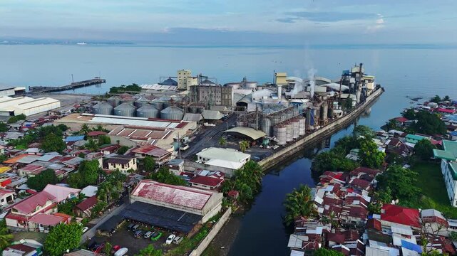Factories line the Cagayan de Oro coastline, pumping thick smoke into the sky beside squatted shanty homes, highlighting industrial pollution and social disparity.