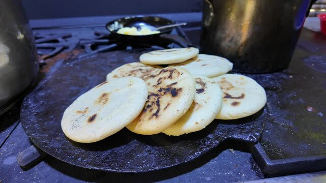 Freshly made arepas cooking on a traditional cast-iron budare, crispy and golden