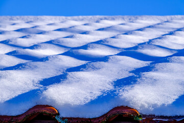 Snow covers a textured roof with bright blue sky in the background during winter season...