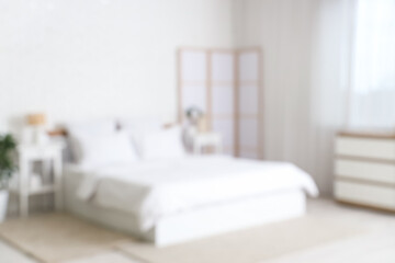 Blurred view of stylish bedroom with cozy bed, soft pillows and folding screen