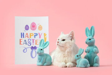 Cute white cat with toy rabbits and greeting card on pink background. Easter celebration