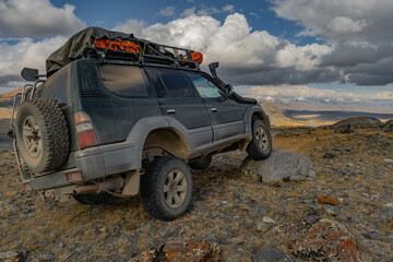 A family off-road touring car, on an off-road mud rubber, drove over a large stone, which is located on an elevated mountain. The mud rubber hit the object.