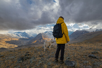 A traveler in bright clothes with a backpack on his back, walks with his pet in the mountains...