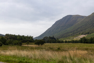 Golden sunset over calm lakes and clear water reflections in The Trossachs and Loch Lomond. Long winding roads cross green hills and mountains in a peaceful, awe-inspiring natural landscape. Exploring