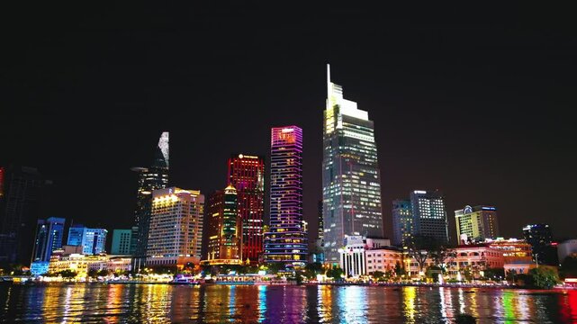 night view of illuminated Ho Chi Minh city skyline and Saigon river, neon street lights of financial downtown district with tall skyscraper towers, Vietnam aerial drone view