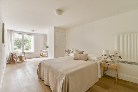 A bright, airy bedroom featuring a simple bed, minimal decor, and large windows allowing natural light. The neutral tones create a peaceful atmosphere.