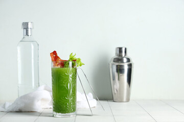 Glass of green bloody mary cocktail with bacon and celery on white tile table