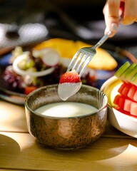 Fresh strawberry forking into creamy dip gourmet food scene rustic dining sunny outdoor setting captivating culinary experience