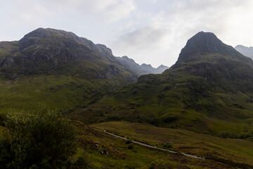 Golden sunset over calm lakes and clear water reflections in The Trossachs and Loch Lomond. Long winding roads cross green hills and mountains in a peaceful, awe-inspiring natural landscape. Exploring