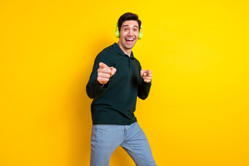 Cheerful Man in Green Polo Shirt and Headphones Posing Against a Vibrant Yellow Background for...