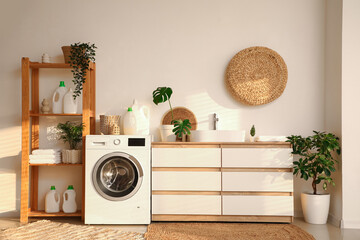 Stylish laundry room with modern washing machine, dresser, sink and bottles of detergent