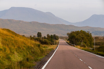 Golden sunset over calm lakes and clear water reflections in The Trossachs and Loch Lomond. Long winding roads cross green hills and mountains in a peaceful, awe-inspiring natural landscape. Exploring