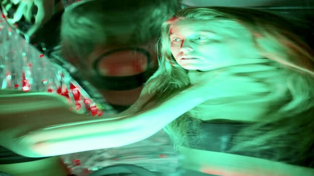 Young artistic woman giving dramatic surreal performance, screaming and expressing intense emotion beside distorting mirror under multicolored neon lights