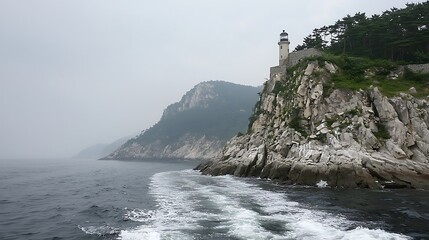 Fototapeta premium Lighthouse on rocky cliff, misty sea.